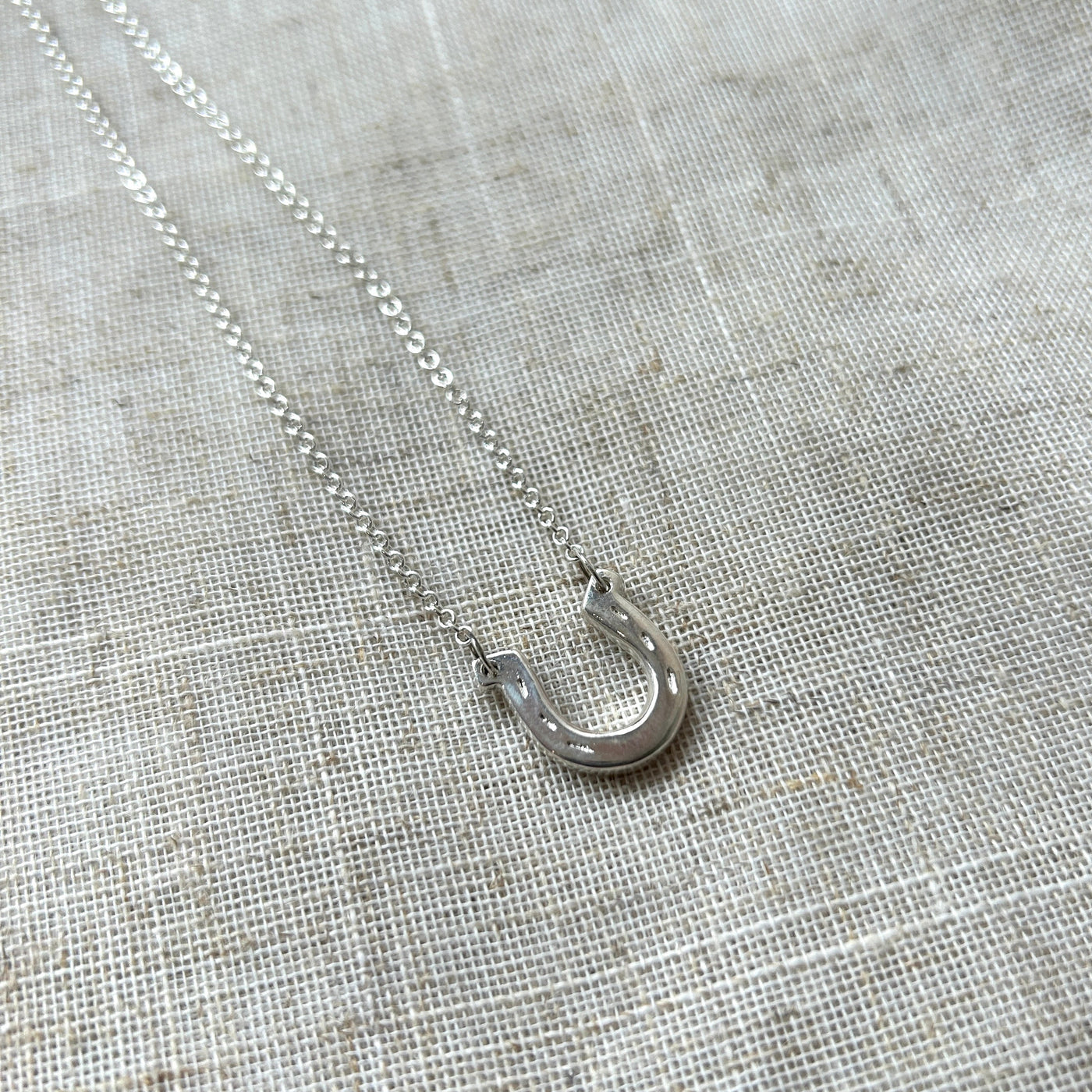 Silver necklace with a small pendant on a textured gray fabric background