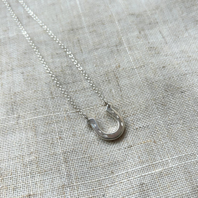 Silver necklace with a small pendant on a textured gray fabric background