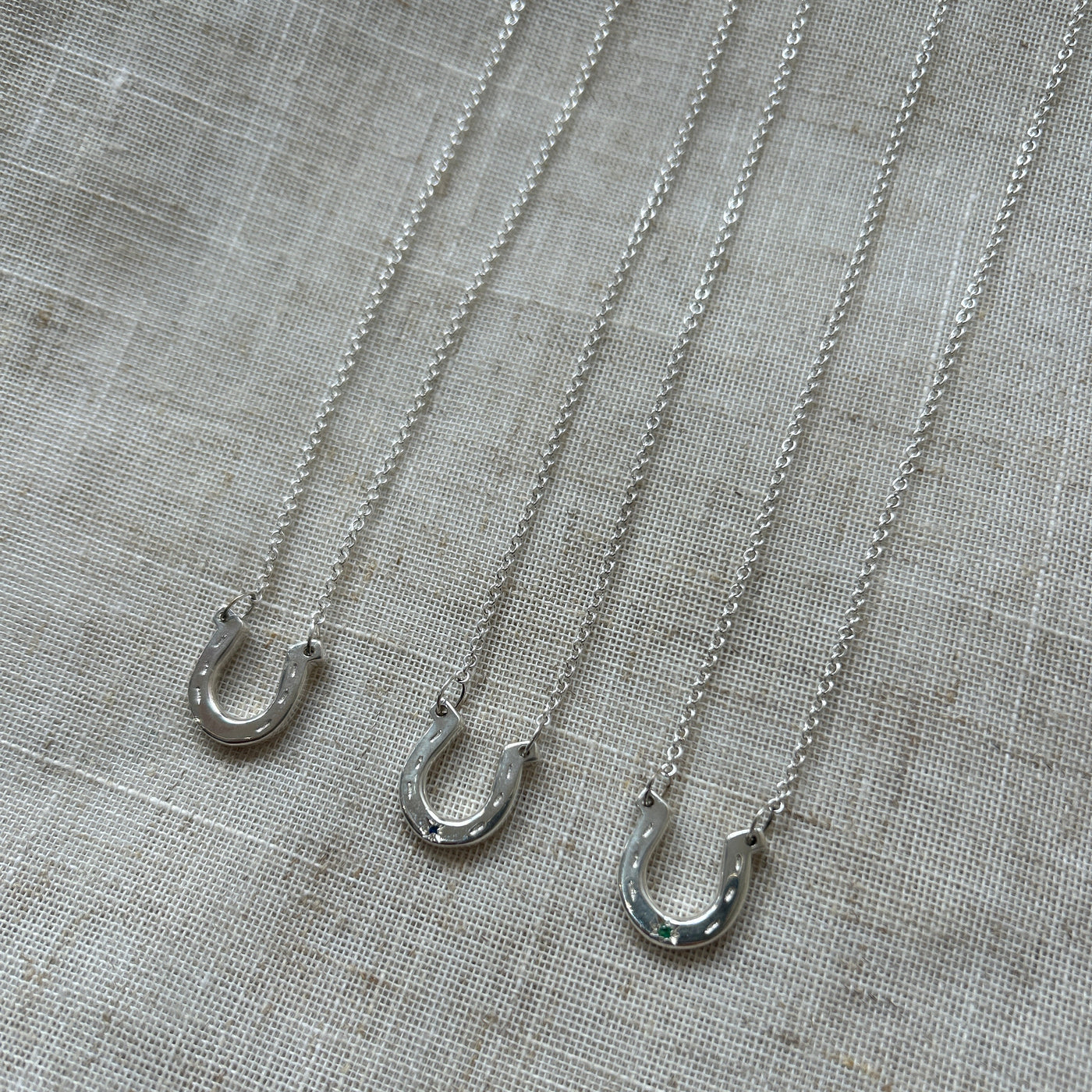 Three silver horseshoe charms on trace chains on a textured grey fabric background