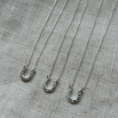 Three silver horseshoe charms on trace chains on a textured grey fabric background