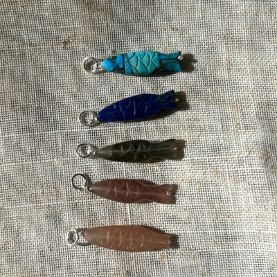Set of five colourful gemstone fish pendants on a textured fabric background