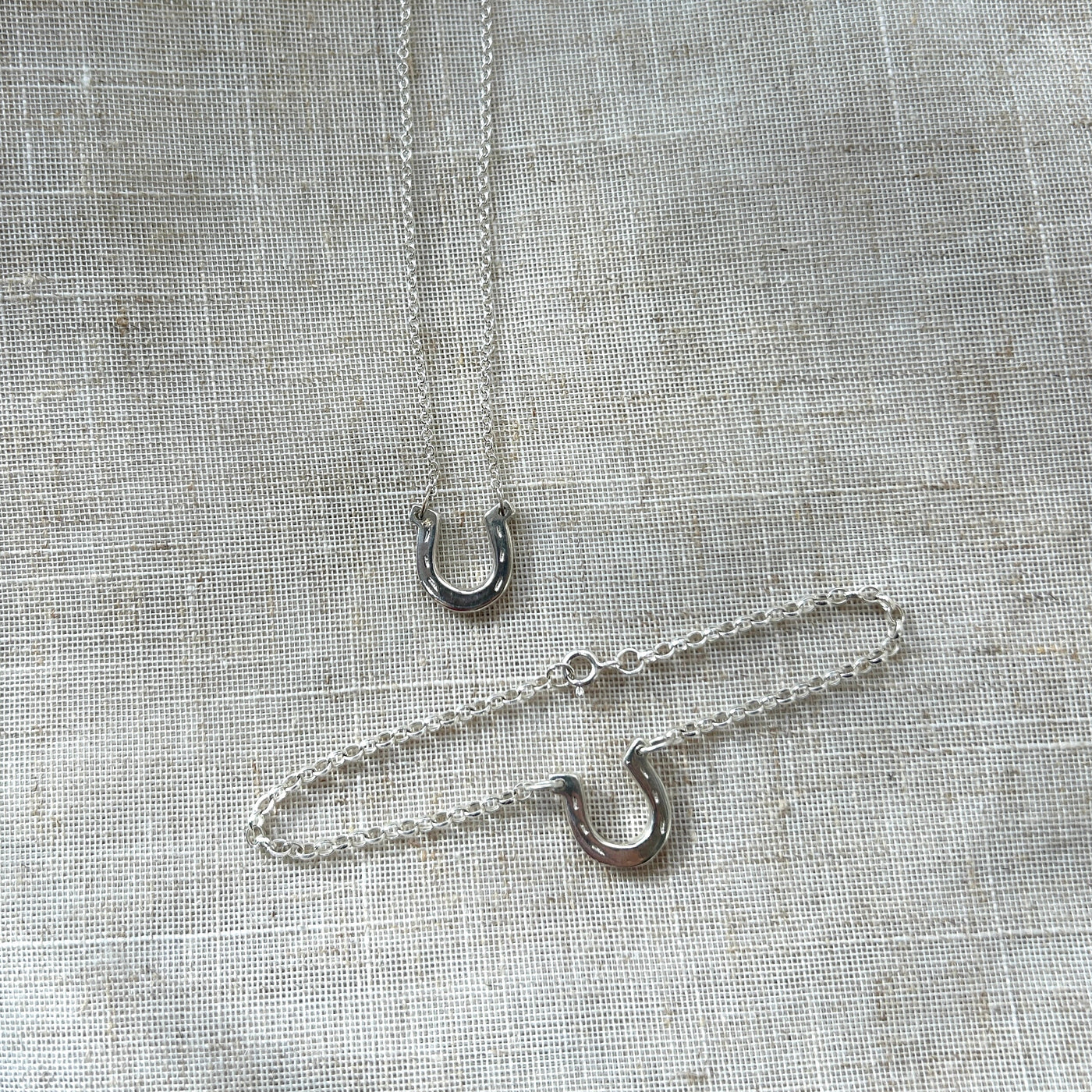 Two silver necklaces with horseshoe charms on a textured gray fabric background