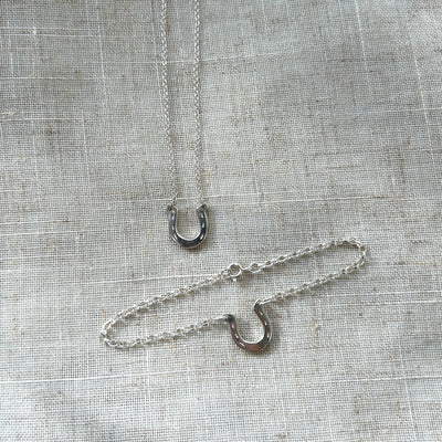 Two silver necklaces with horseshoe charms on a textured gray fabric background