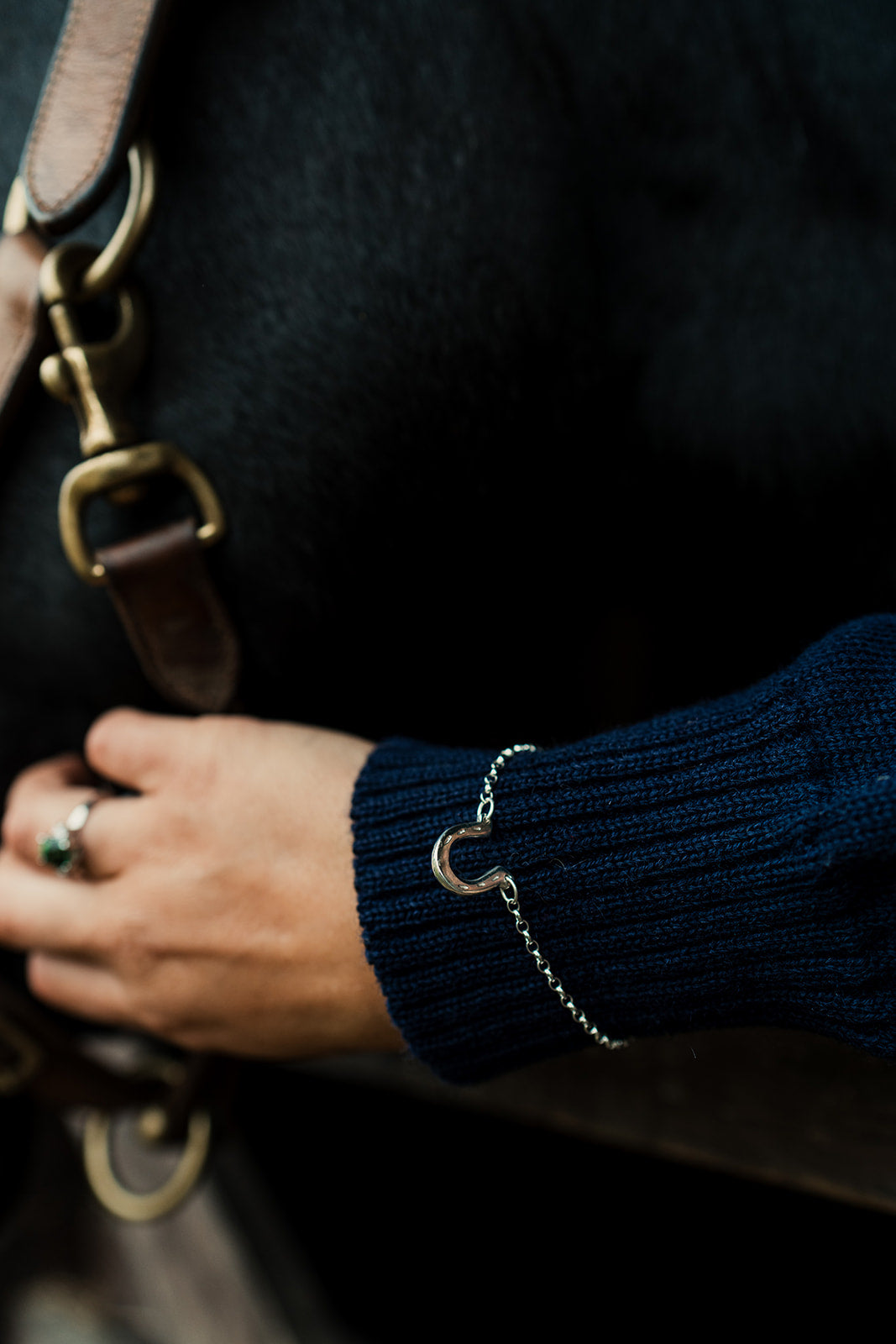 Person wearing a dark blue sweater with a bracelet, holding a leather bag.