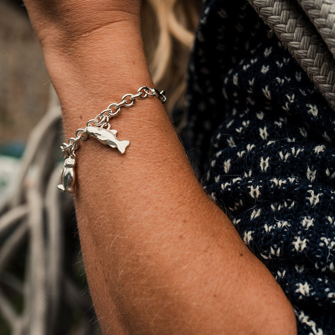 Close-up of a wrist wearing a silver bracelet with a dog tag, against a blurred background.