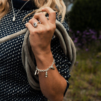 Person holding a rope with a silver sea themed charm bracelet on.