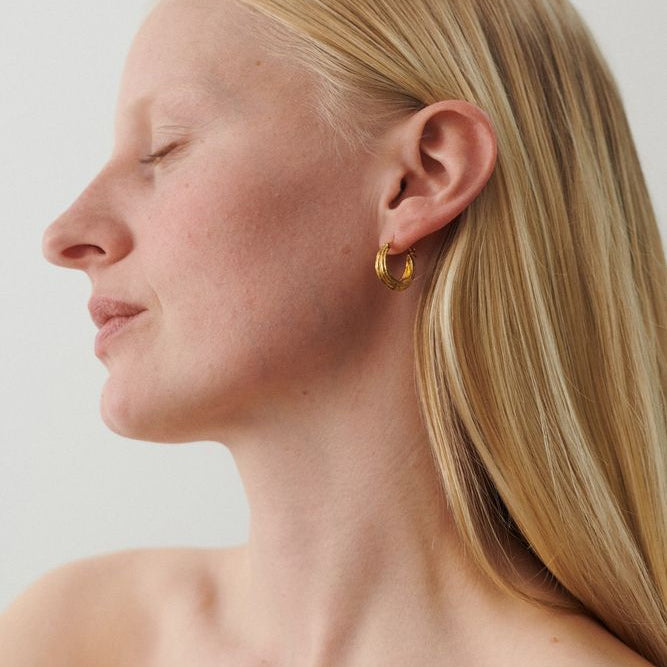 Close-up of a person wearing gold earrings with a plain background