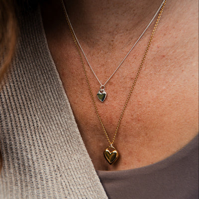 Close-up of a person wearing multiple necklaces with heart pendants.