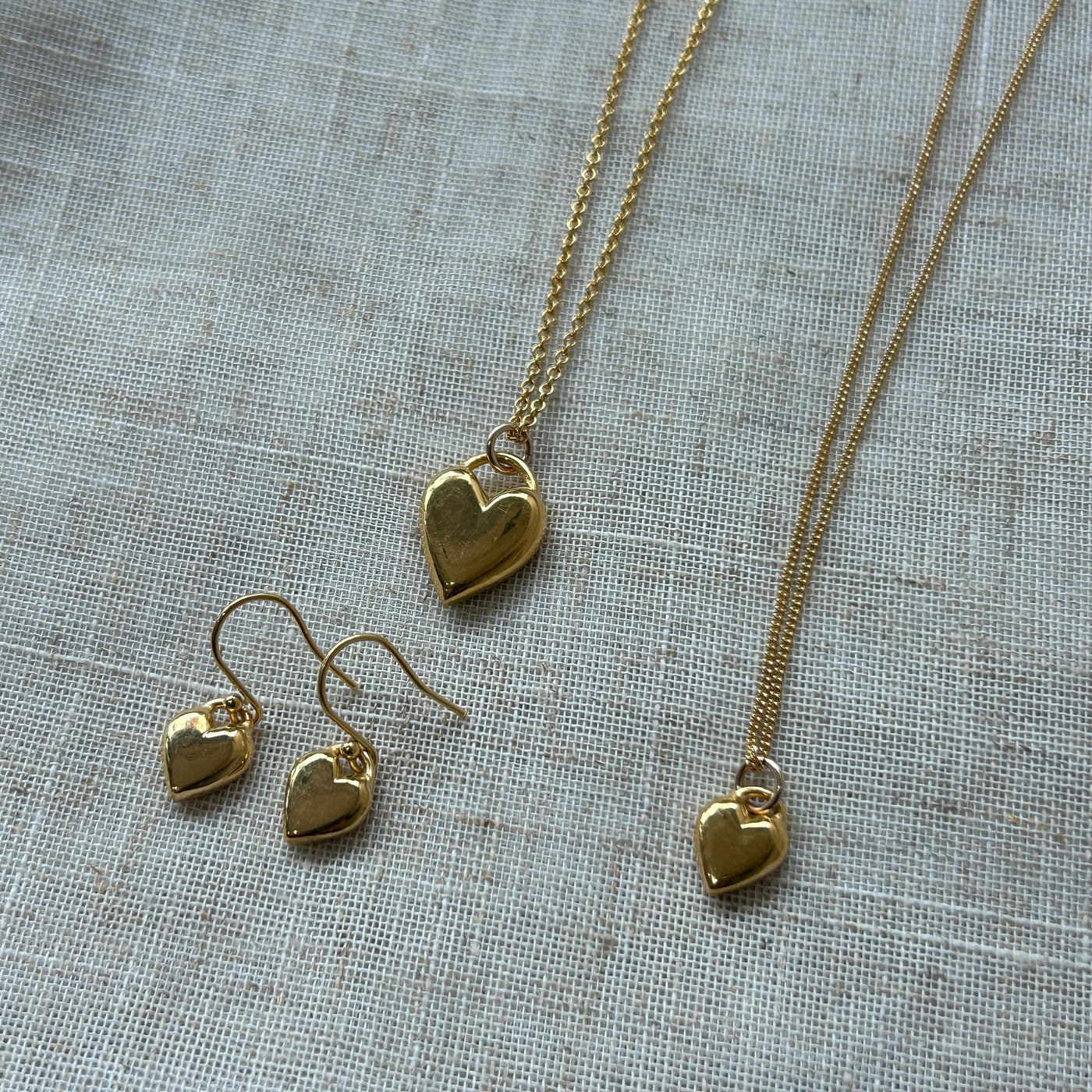 Gold heart-shaped jewelry set on a textured fabric background