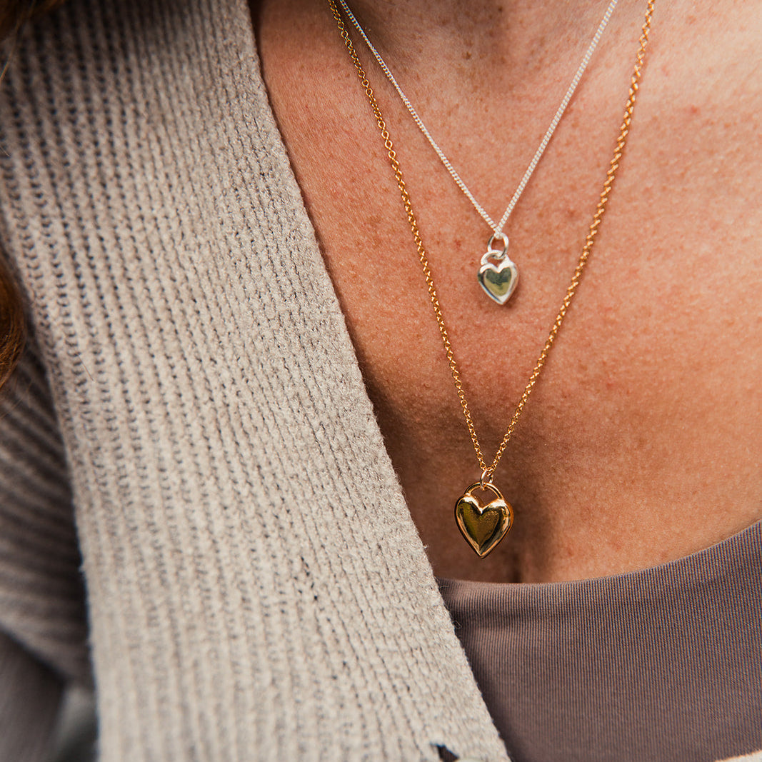 Close-up of a person wearing two gold heart-shaped pendant necklaces.