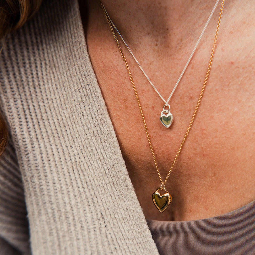 Close-up of a person wearing two gold heart-shaped pendant necklaces.