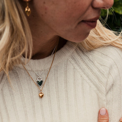 Woman wearing a beige sweater and gold jewelry, holding pink flowers.