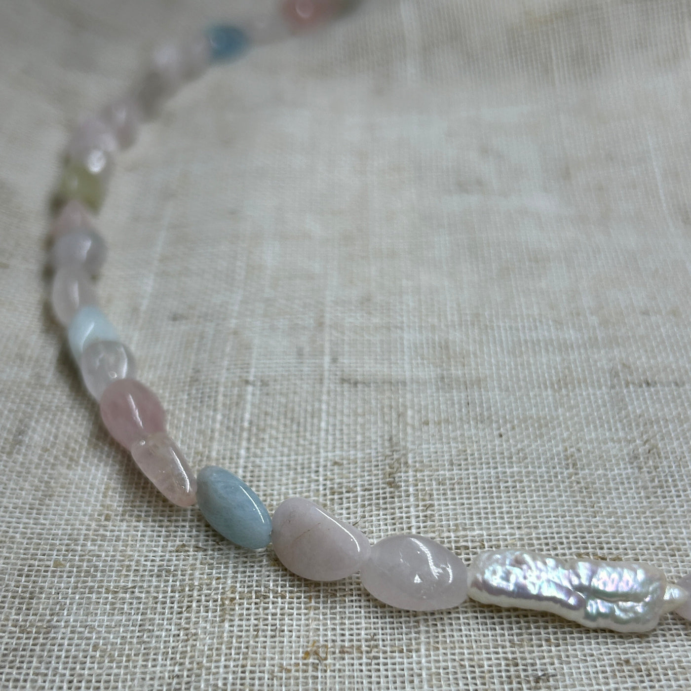 Necklace with light blue and clear beads on a textured fabric background