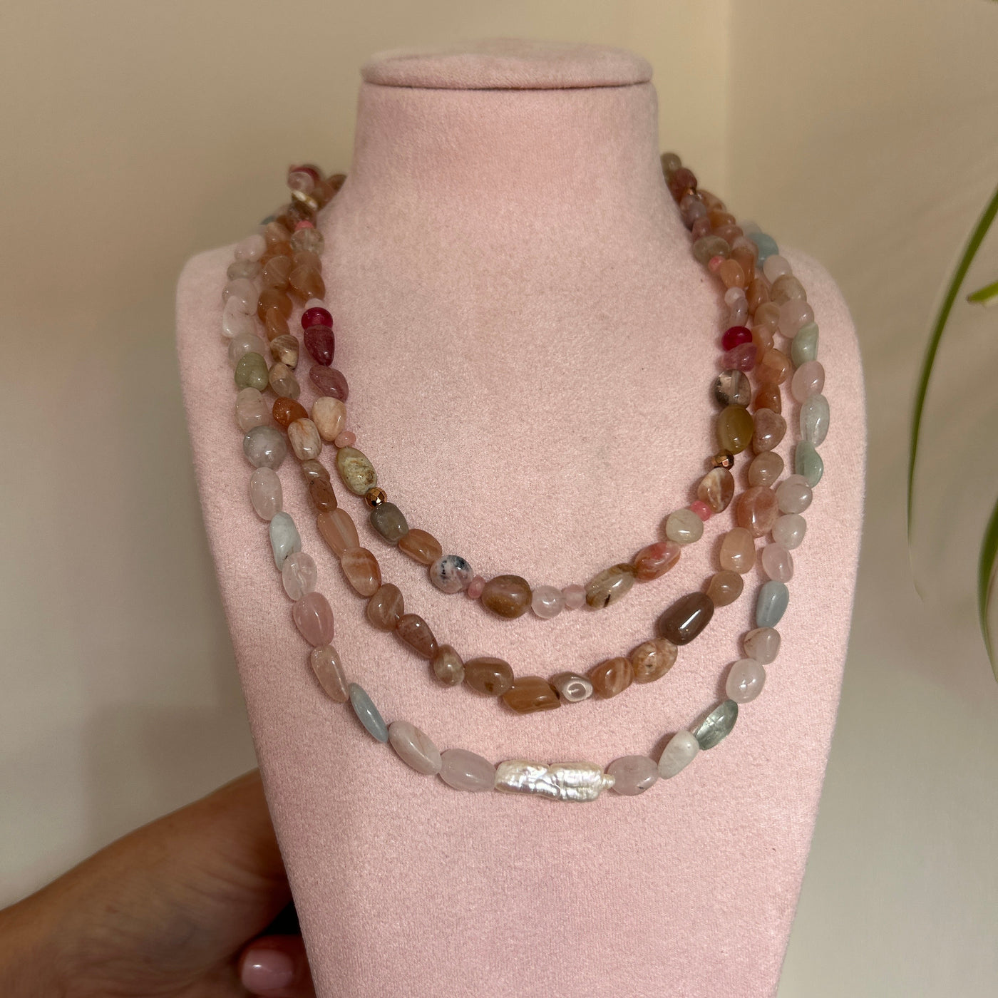 Three beaded bracelets on a pink velvet stand held by a hand.
