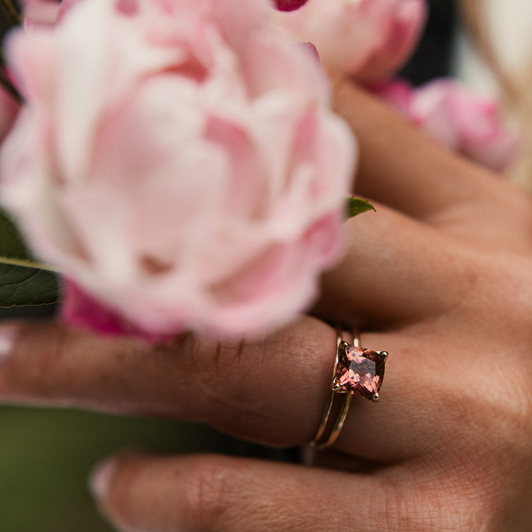 Pink cushion cut tourmaline gem in yellow gold ring on a woman's hand holding a pink rose
