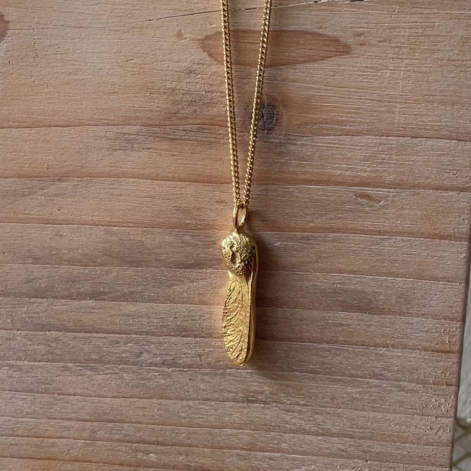 A video of a gold sycamore gap seed pendant on a gold curb chain on a wooden block background made in Northumberland 