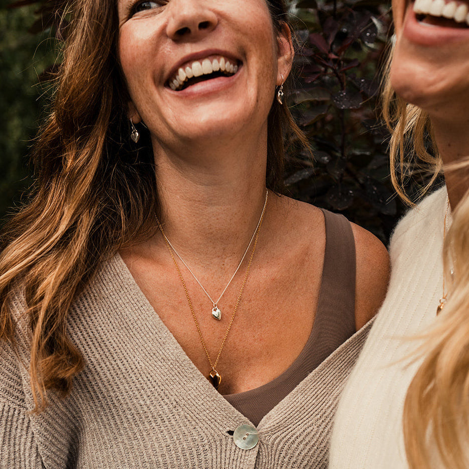 Two women laughing outdoors, one wearing a beige cardigan.