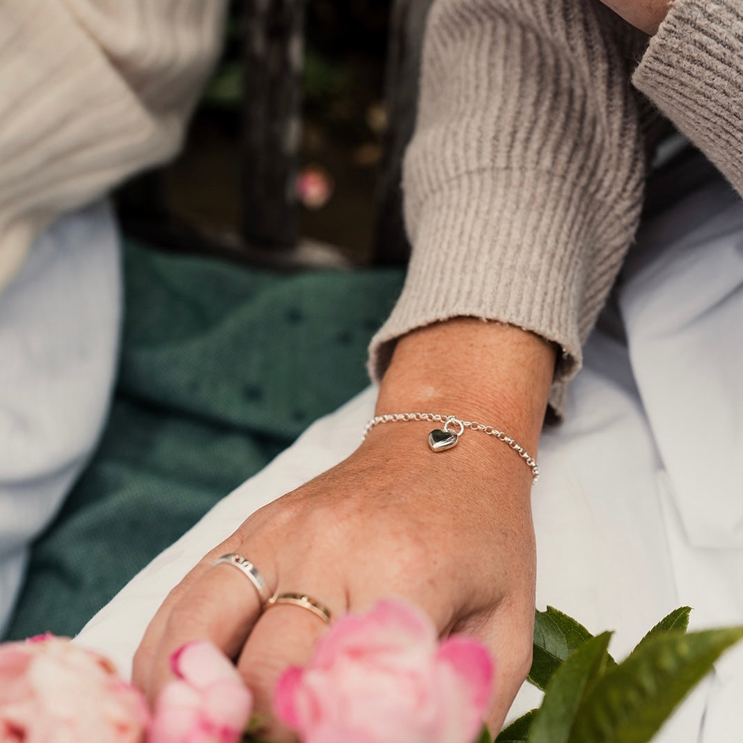 Woman wearing a silver heart bracelet and rings with pink flowers in a natural setting