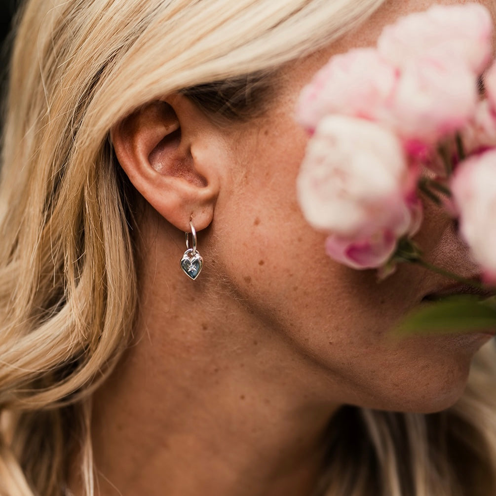 Close-up of a woman wearing an earring with pink flowers in the background