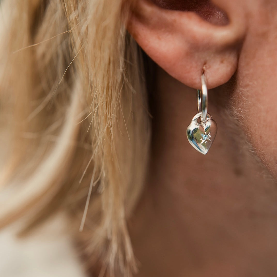 Close-up of a person wearing a silver heart-shaped earring with a blurred background