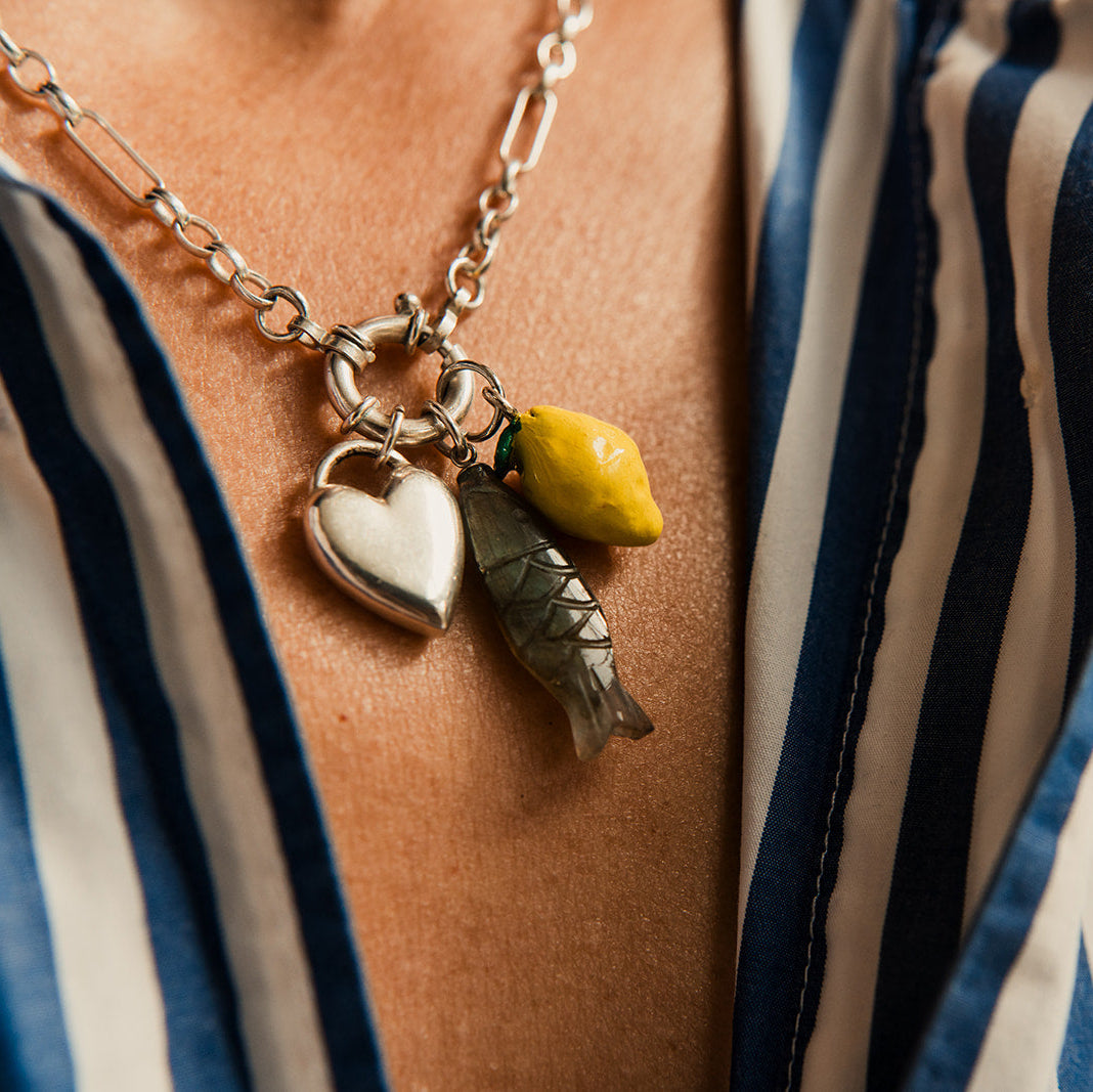 Necklace with heart, fish and lemon charm worn by a person in a striped shirt.