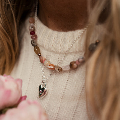 Close-up of a person wearing a necklace with a heart pendant, holding pink flowers.