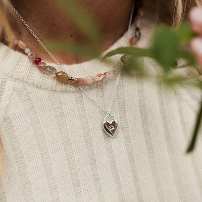 Silver heart pendant with star set ruby on silver chain worn by a woman with blonde hair and a cream jumper