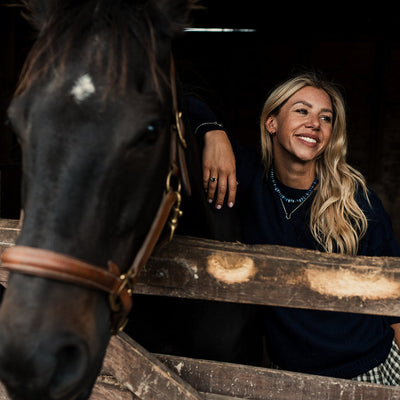 Woman standing next to a horse in a stable wearing a silver horseshoe pendant