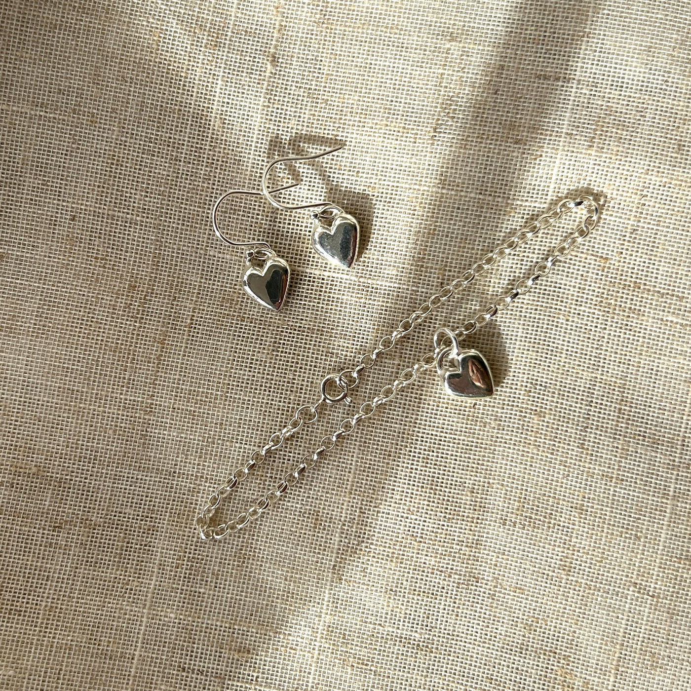 Silver heart-shaped jewelry set on a textured beige fabric background