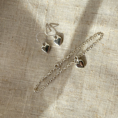 Silver heart-shaped jewelry set on a textured beige fabric background