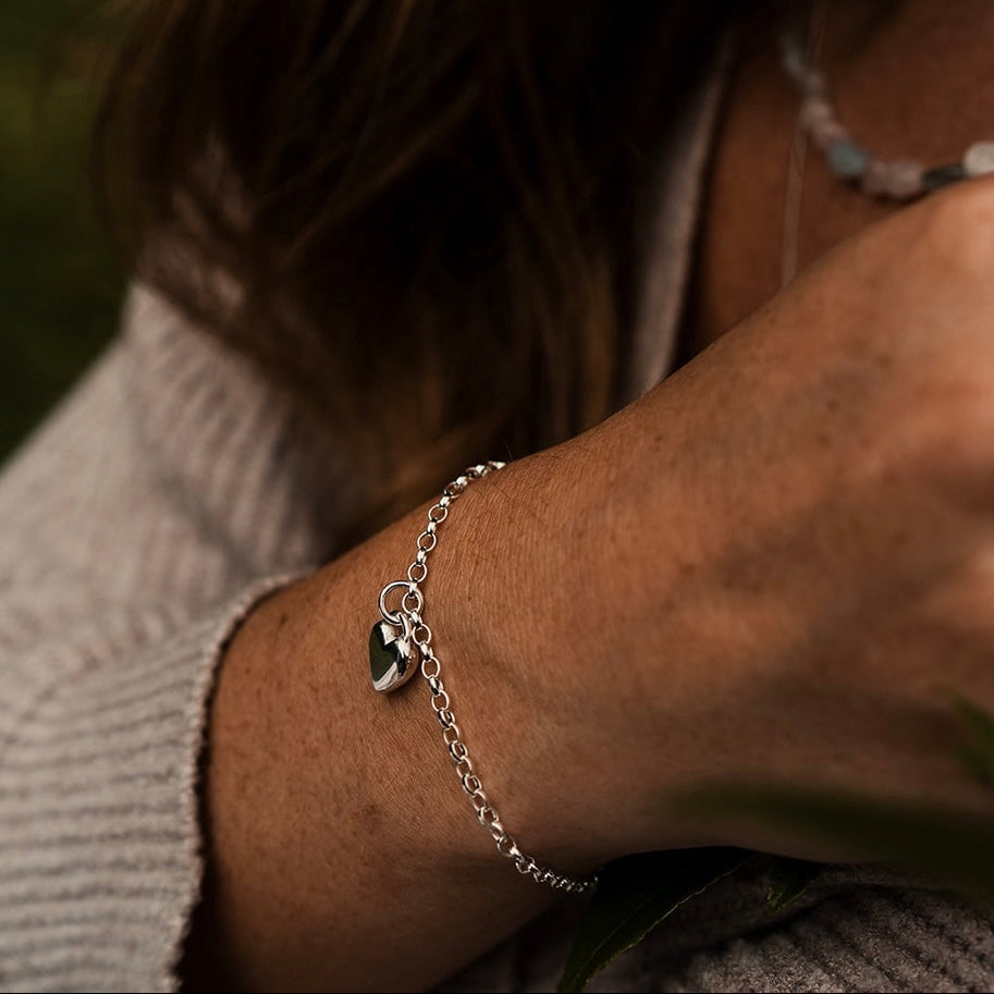 Close-up of a person's wrist wearing a silver bracelet with a heart charm, blurred background