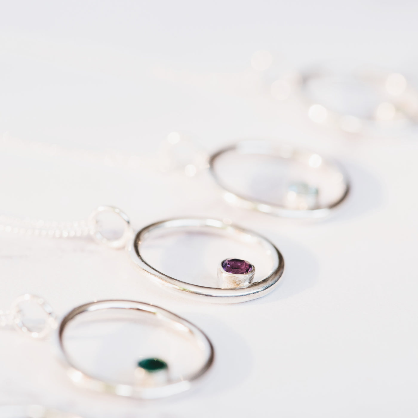 Four silver wire circle pendants in a rose offset with faceted round gemstones and silver trace chain on a white background