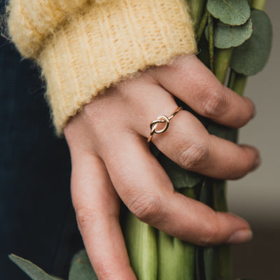 Yellow gold wire tied in a knot ring worn on the ring finger as a promise ring. the model is holding a bunch of flowers with yellow cuff jumper, handmade Kirsty Taylor Goldsmiths, Corbridge Northumberland, promise ring